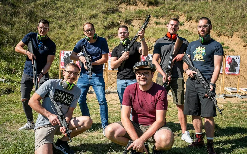 Skupina pózuje s instruktory na venkovní střelnici