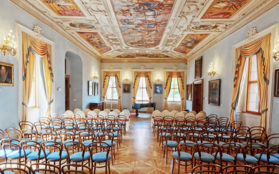 Rows of concert chairs beneath a decorated palace ceiling